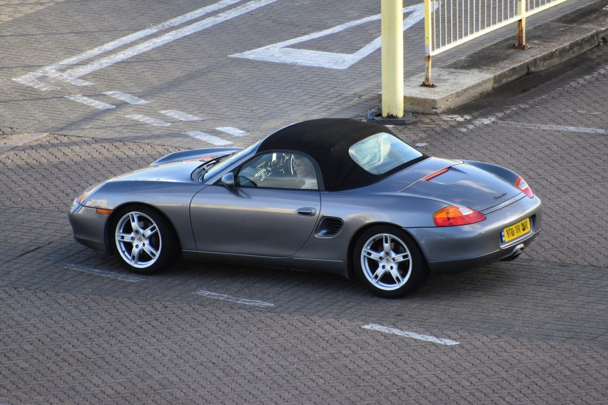 Silver 2001 Porsche Boxster 986 with the black soft top up, side and rear three-quarter view